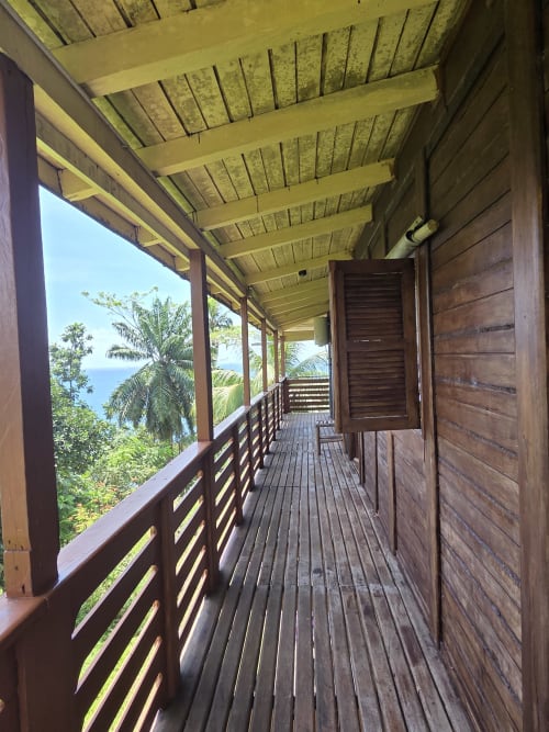 Varanda de madeira com corrimão com vista para jardins tropicais e o mar em Equador Houses, São Tomé