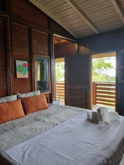 Quarto espaçoso na Equador Houses São Tomé com vista para o mar, móveis de madeira, almofadas laranja e varanda virada para o oceano