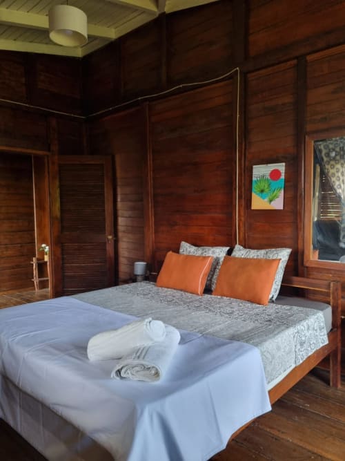 Quarto de madeira com vista para o oceano na Equador Houses, São Tomé, com duas camas, almofadas laranja e toalhas brancas