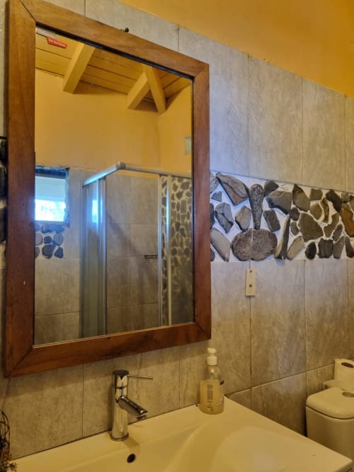 Banheiro da Equador Houses Vila Paraíso em São Tomé com pia branca, espelho com moldura de madeira e destaque em azulejo decorativo