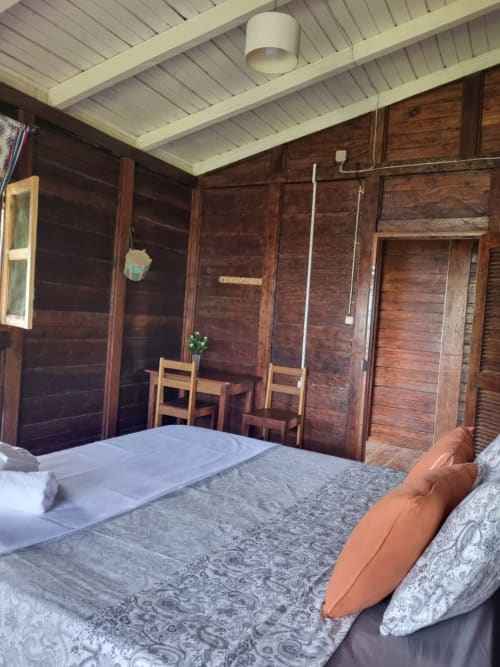 Quarto de madeira da Vila Paraíso, Casarões São Tomé no Equador, com cama, cadeira e teto branco