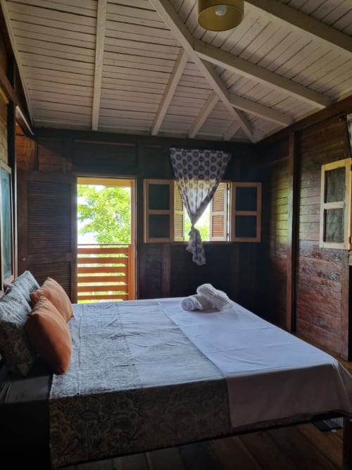 Quarto em Vila Paraíso na Ecuador Houses, São Tomé com cama de casal, móveis de madeira e vista para o mar da varanda