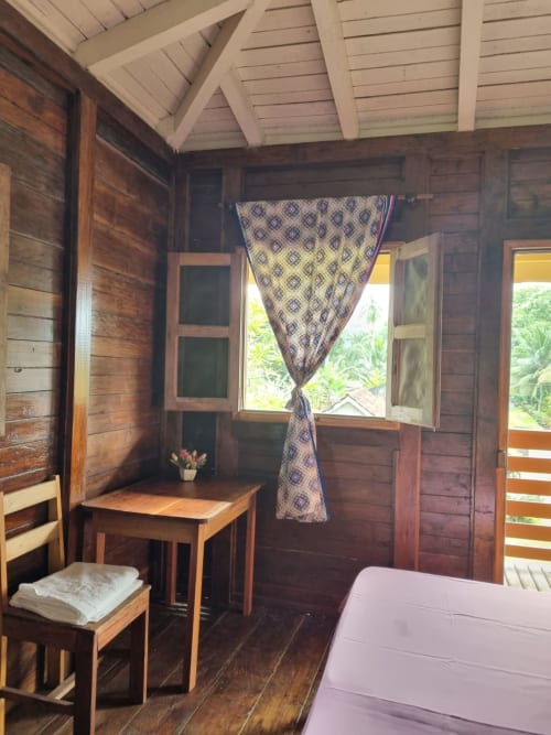 Quarto de madeira na Equador Houses, São Tomé com cortina estampada, escrivaninha, cadeira e vista para o mar