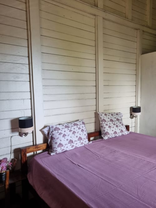 Roupa de cama roxo e branco no quarto duplo Vila Paraíso da Equador Houses, São Tomé, com paredes de ripas de madeira