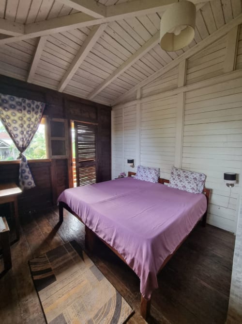 Quarto com lençol rosa na Equador Houses Vila Paraíso, São Tomé, com móveis de madeira e teto branco