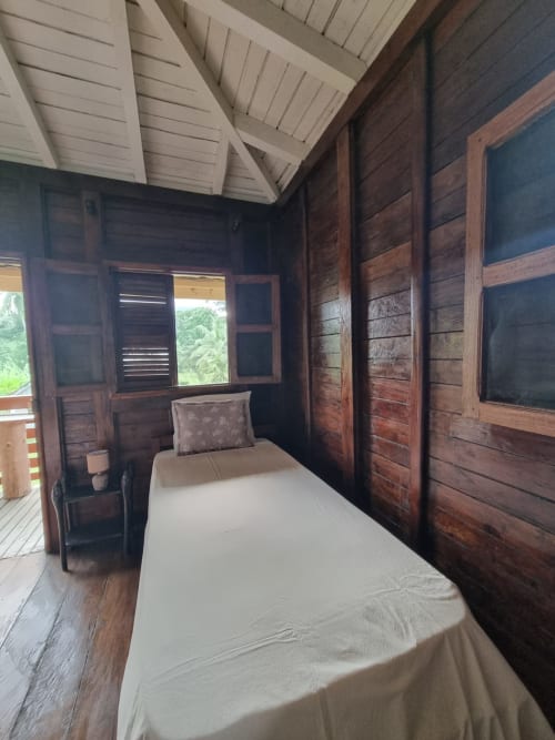 Quarto aconchegante com cama de solteiro, paredes em madeira escura e vista para o mar na Equador Houses, São Tomé