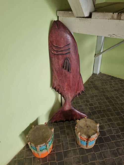 Escultura tradicional de peixe em madeira com tambores expostos na sala Vila Paraíso das Casas do Equador, São Tomé