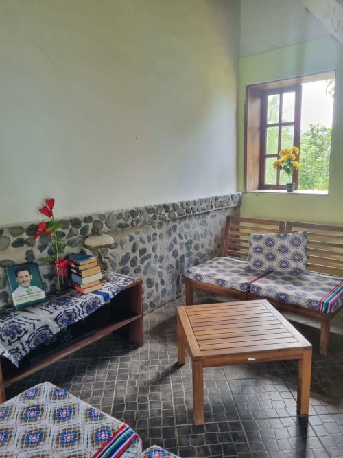 Quarto aconchegante na Equador Houses em São Tomé com camas de madeira, parede de pedra, flores amarelas e vistas do jardim