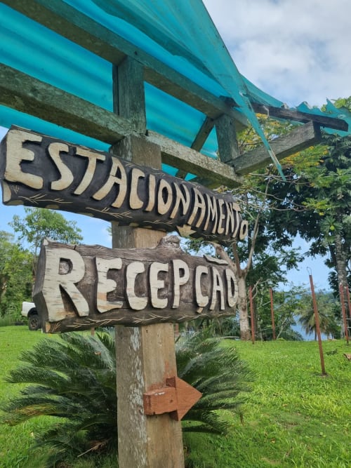 Placas de madeira indicando Estacionamento e Recepção nas Casas Equador em São Tomé, com pérgolado turquesa acima