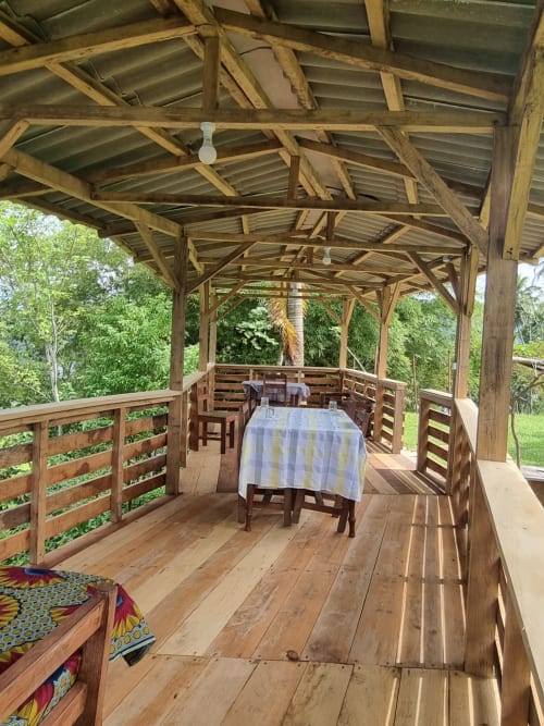 Varanda coberta em madeira na Equador Houses em São Tomé, com mesa de jantar, cadeiras e vistas do exuberante jardim