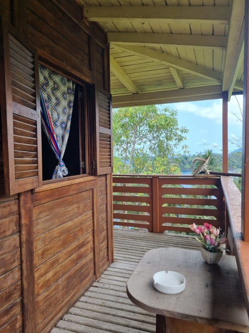 Varanda de madeira em Equador Houses com vista para o mar e jardins exuberantes em São Tomé, com mesa, flores rosas e venezianas abertas