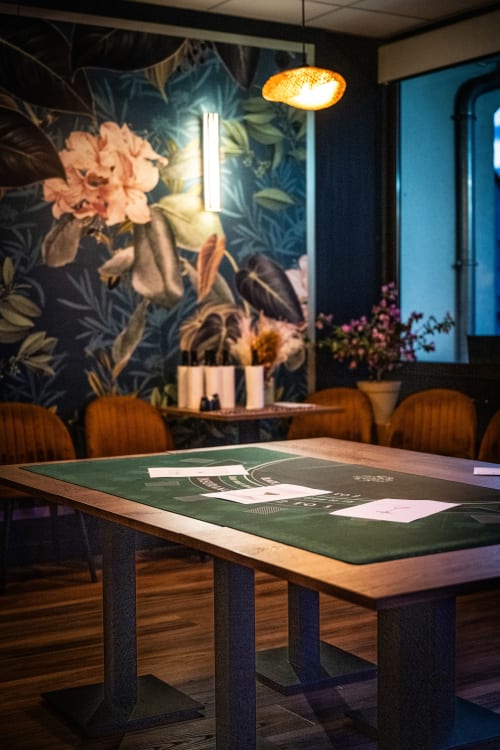Modern conference room at Hôtel Restaurant Le S'Y with green table, wooden chairs, floral mural, and warm lighting.