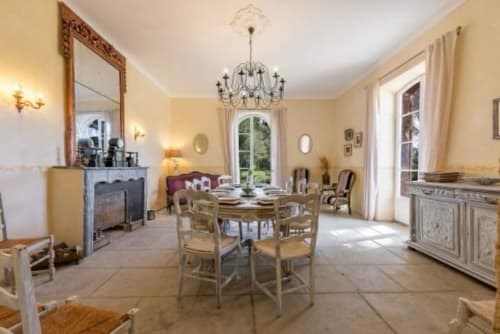 Élégante salle à manger du Château de Sienne avec table ronde, lustre, cheminée et vue sur le jardin à Chusclan