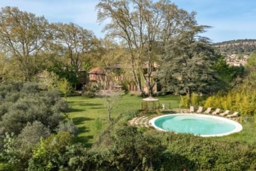 La piscine chauffée du Château de Sienne entourée de jardins soignés, d'oliviers et d'une villa de campagne rustique à Chusclan