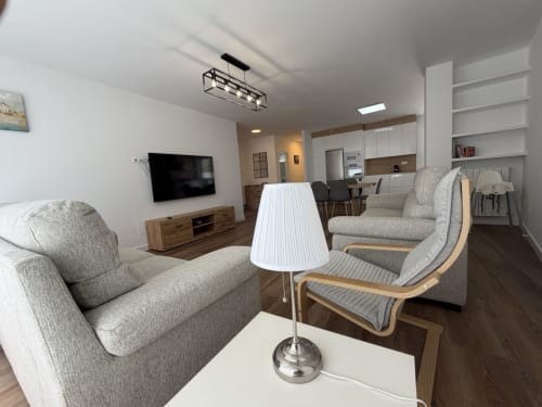 Moderna sala de estar abierta en Bahia de Santoña con asientos beige, televisor, cocina y comedor en Santoña