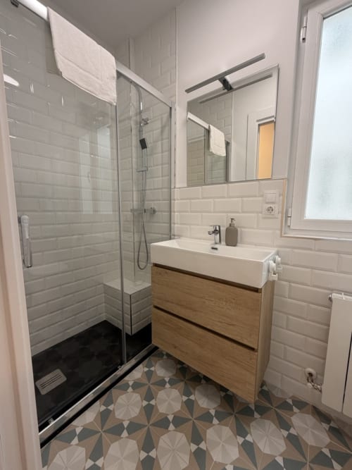Baño moderno en Alojamientos Bahía de Santoña con ducha abierta, mueble de madera y baldosas geométricas