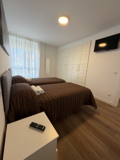 Habitación moderna en Alojamientos Bahía de Santoña con dos camas, TV mural, armarios empotrados blancos y cortinas translúcidas