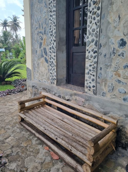 Banco de madeira rústica na entrada da villa de pedra em São Tomé com jardim vista para o mar