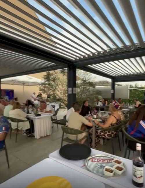 Outdoor terrace at Hôtel Restaurant Le S'Y with guests dining under modern pergola with adjustable louvers