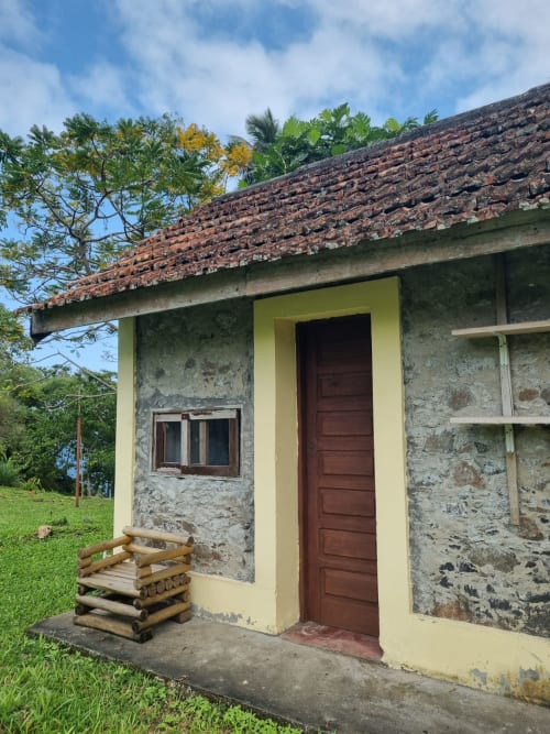 Aconchegante chalé de pedra com detalhes amarelos e telhado de tijolos vermelhos na Equador Houses, São Tomé, com banco de madeira e vista para o mar