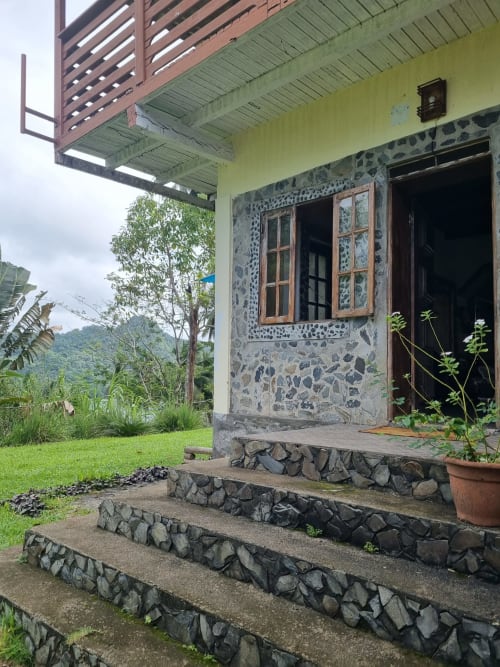 Exterior do quarto Vila Paraíso em São Tomé com degraus de pedra, fachada verde-limão, janela de madeira, vista do jardim e montanha
