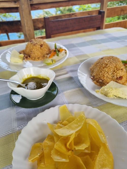 Mesa de café da manhã nas Casas Equador São Tomé: arroz frito, limão fresco, sopa e pastéis no terraço de madeira