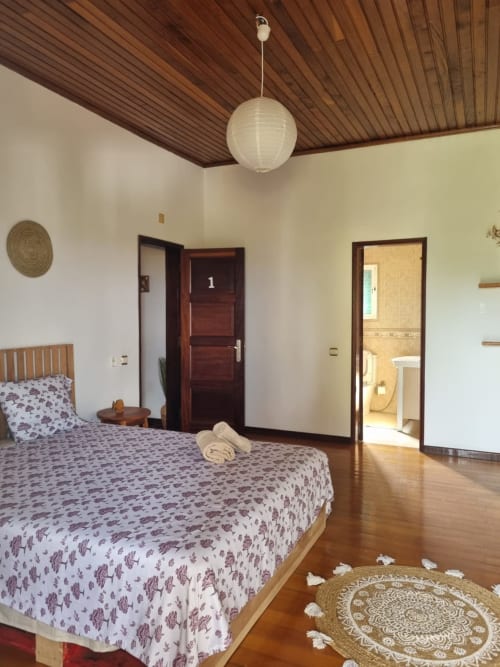 Quarto de casal espaçoso nas Equador Houses em São Tomé, com teto de madeira, vista para o oceano e casa de banho privada.