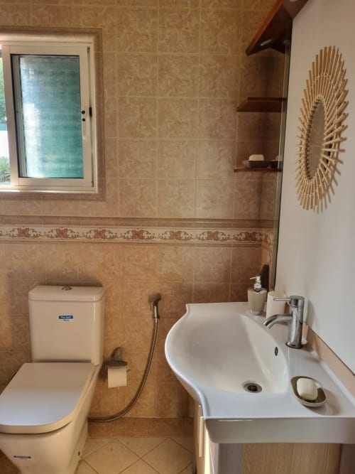 Banheiro moderno nas Equador Houses, São Tomé com azulejos bege, fixtures brancos, pia, vaso sanitário e espelho decorativo