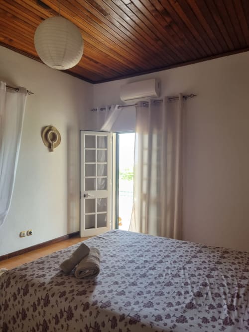 Quarto luminoso na Equador Houses São Tomé com teto de madeira, cama de casal, ar condicionado e portas de vidro com vista para o balcão do oceano