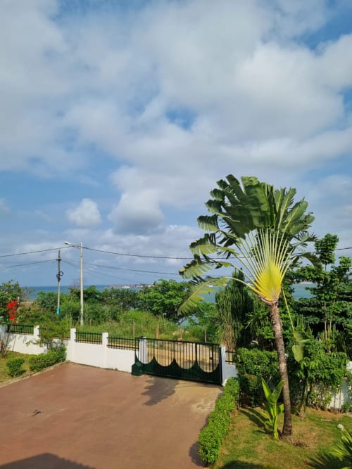 Entrada da mansão Equador com jardim tropical, vista para o oceano além, São Tomé