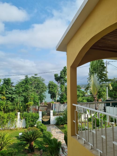 Varanda amarela com corrimão branco oferecendo vista panorâmica para jardim tropical e oceano em Equador Houses, São Tomé