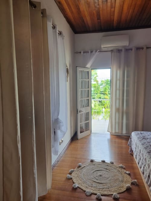 Quarto espaçoso na Equador Houses em São Tomé com teto de madeira, tapete redondo, guarda-roupa e portas francesas que se abrem para o jardim