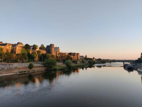 L'hôtel fluvial Château Haute Roche à Oudon, France avec ses bâtiments historiques en briques se reflétant dans l'eau calme au coucher du soleil