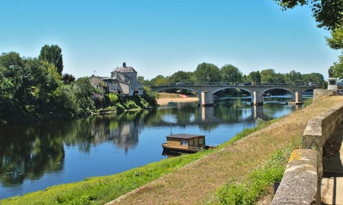 Chateau Haute Roche overlooks the Oudon river with a moored boat, stone bridge, and green countryside.