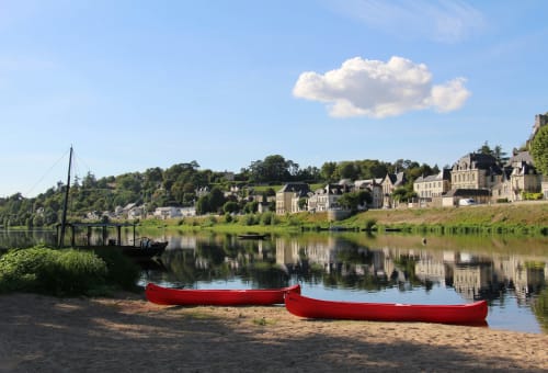 Red boats on sandy beach by Oudon river with Chateau Haute Roche and French village reflected in calm water
