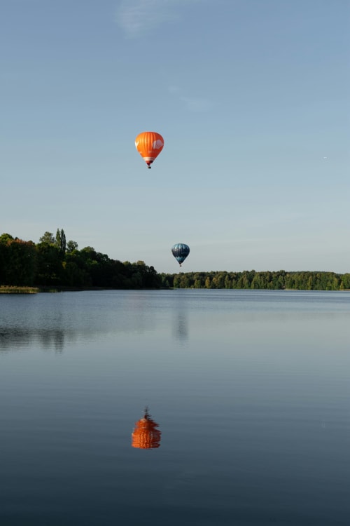 Hot air balloons floating above calm lake with forest at Chateau Haute Roche, Oudon