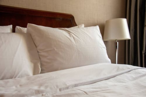 Literie et oreillers blanc immaculé sur un lit de l'hôtel L'escapade au Mans avec lampe de chevet et tête de lit sombre