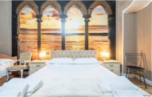 Camera elegante presso Yaki Domo B&B a Cagliari con finestra ad arco, vista sul mare al tramonto, letto bianco e comfort moderni