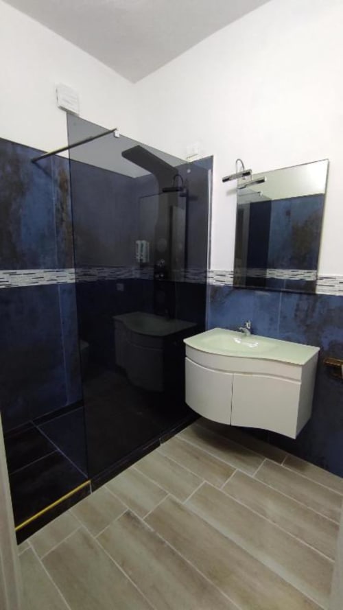 Bagno moderno presso Yaki Domo Cagliari con piastrelle blu scuro, lavabo bianco e doccia in vetro