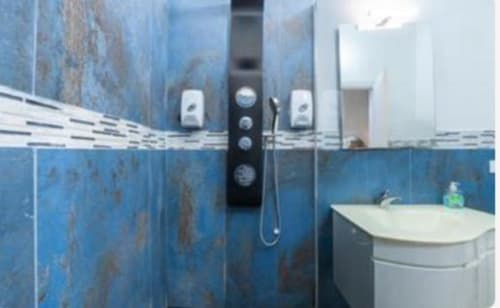 Bagno moderno nella camera Yaki Domo Platinum a Cagliari con piastrelle blu in rilievo, sistema doccia e vanity bianco.