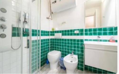 Bagno moderno con piastrelle verdi, sanitari bianchi, doccia e bidet nella camera Yaki Domo Gold, Cagliari