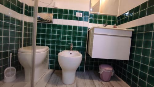 Bagno moderno presso Yaki Domo B&B Cagliari con piastrelle verdi, wc bianco, bidet, lavabo e mobile sottolavabo