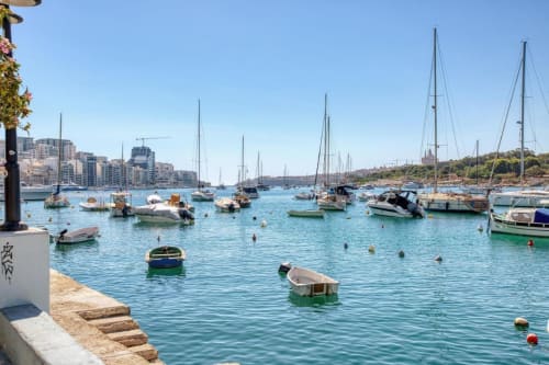 Porto mediterraneo turchese a Sliema, Malta con barche a vela ormeggiate, yacht e edifici sul waterfront sotto cielo azzurro