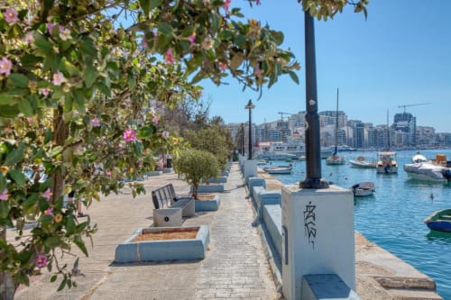 Lungomare della Marea a Sliema con buganvillee fiorite, barche e vista sul porto mediterraneo