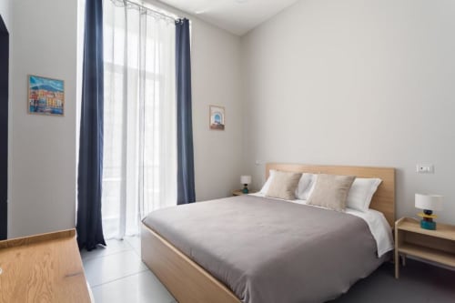 Camera da letto moderna e luminosa presso Darna Rooms Napoli con letto matrimoniale, testiera in legno, tende blu navy e accesso al balcone