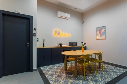 Zona pranzo moderna di Darna Rooms Napoli con insegna neon gialla, tavolo in legno, armadietti scuri e piastrelle decorate