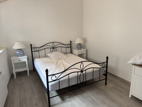 Chambre à Zogbi Hospitality Aubonne avec lit en fer forgé noir, tables de nuit blanches, lampes en céramique bleue et parquet