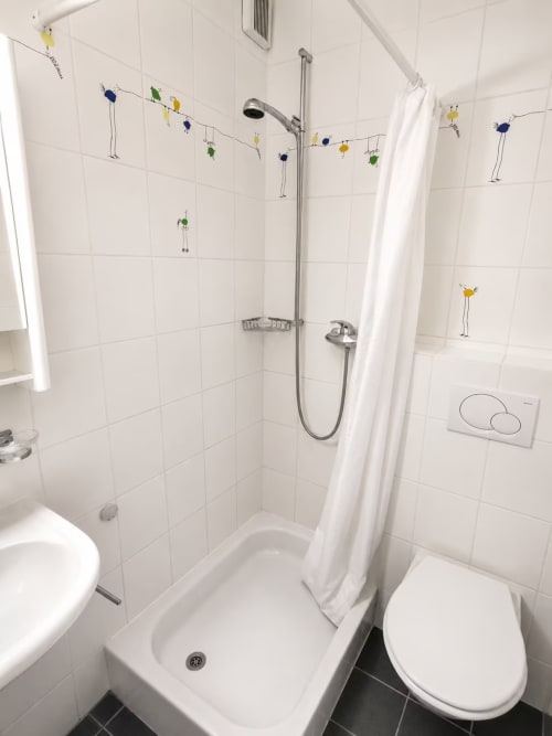 Salle de bain moderne à Zogbi Hospitality Lausanne avec carrelage blanc, douche, toilettes et décoration fantaisiste suspendue