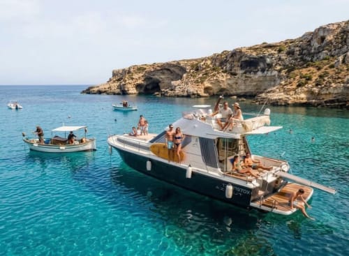 Acque turchesi di Lampedusa con barche e ospiti che godono il Mar Mediterraneo vicino alle scogliere calcaree