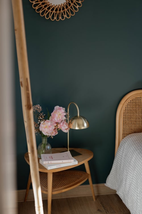 Table de nuit élégante du Manoir de la Nogrie avec pivoines roses, lampe en laiton et livres sur mur bleu-vert